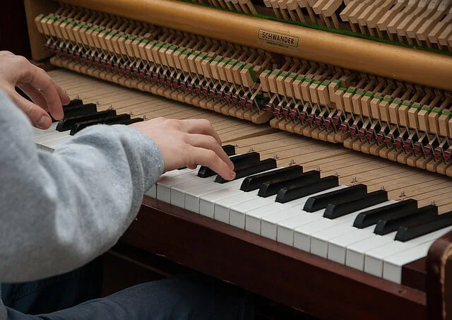 Manos tocando un piano vertical con la mecánica a la vista