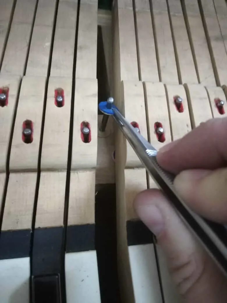 Manos de un técnico ajustando las teclas de un piano con una herramienta, en el taller